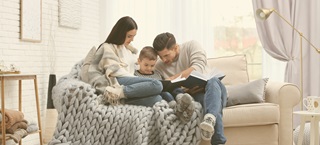 A young family reads on a small couch. This image is for an article about how to prepare for a winter storm in an apartment. The article includes tips on gathering emergency supplies, how to keep perishable foods safe and more.